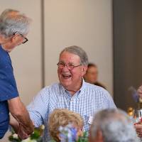 Gentleman sitting at table, shaking hands with another man who came over to say hi